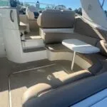 Seating area on a boat with curved beige cushions and a small white table, with steps leading to the cockpit.