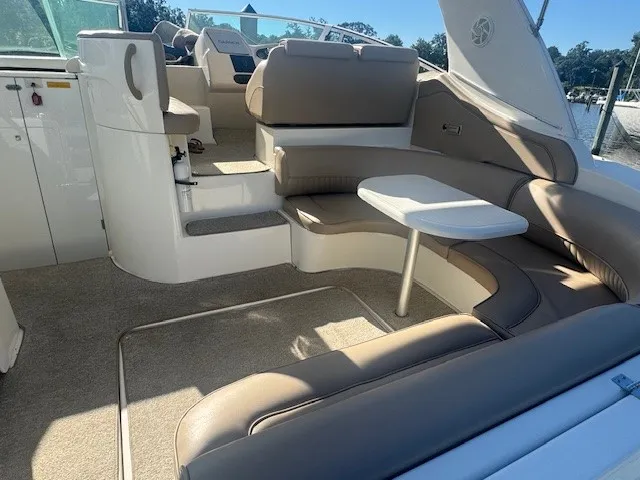 Seating area on a boat with curved beige cushions and a small white table, with steps leading to the cockpit.