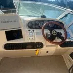 Boat helm with Garmin navigation system, multiple gauges, a wooden steering wheel, and throttle controls.