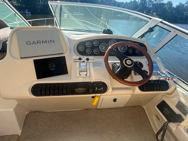 Boat helm with Garmin navigation system, multiple gauges, a wooden steering wheel, and throttle controls.